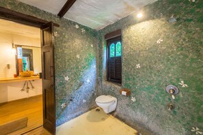 Un baño con paredes de mosaico, inodoro y ventana con contraventanas.
