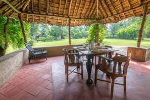 Un porche techado con una mesa y sillas, rodeado de un jardín exuberante y vistas al campo.