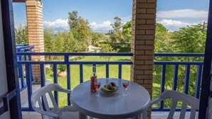 Un balcon avec une table, deux chaises, une bouteille et deux verres contenant une boisson rouge.