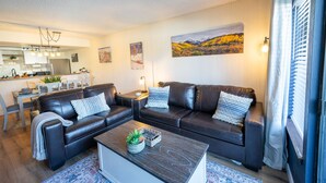 Een moderne woonkamer met twee leren banken, een salontafel en een eethoek, met een keuken op de achtergrond.