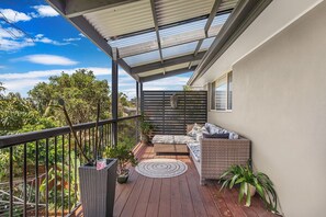 Ein Balkon mit überdachter Sitzecke, Blick auf die umliegende Grünfläche und einen klaren Himmel.