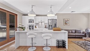Een moderne keuken met een centraal eiland, twee barkrukken, roestvrijstalen apparatuur en hanglampen.