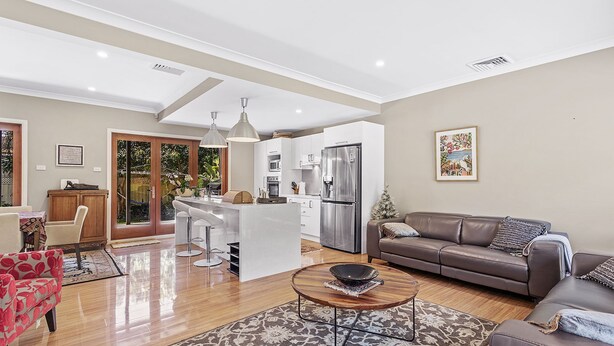 Een moderne woonkamer met een bruine leren bank, een salontafel en een eethoek met witte barkrukken.