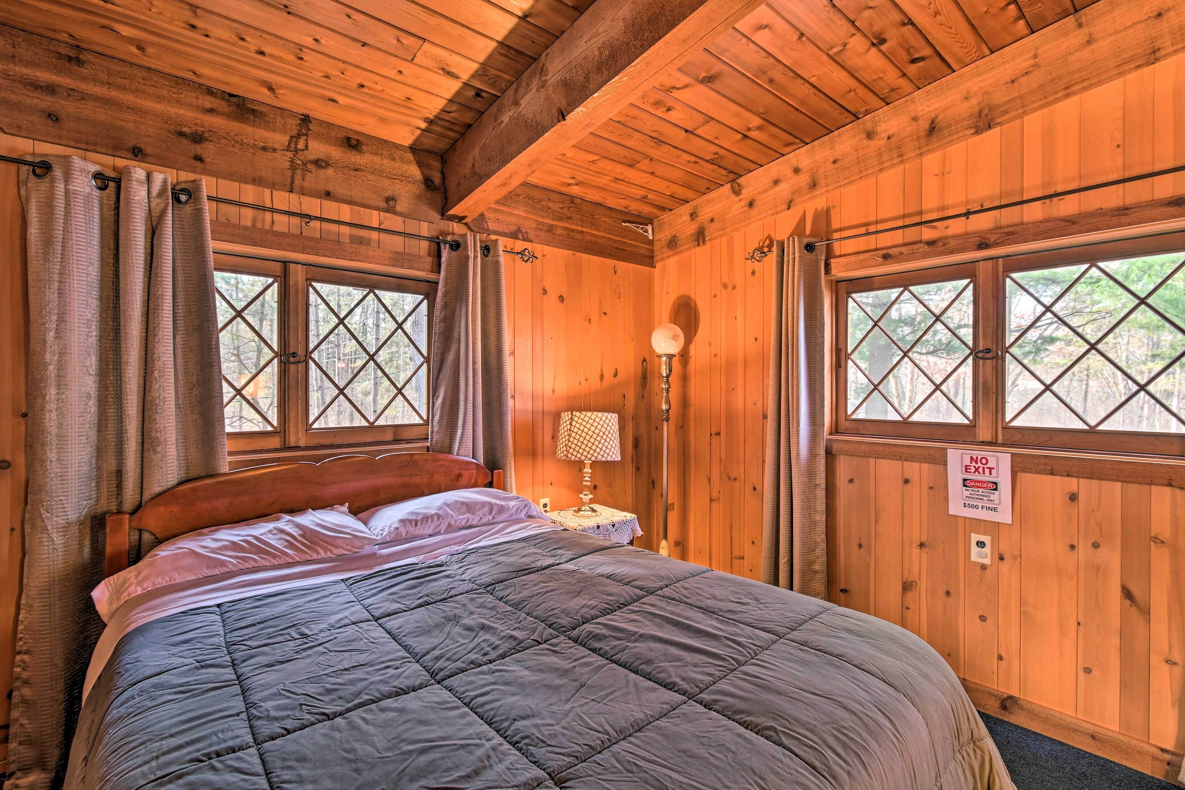 A wooden cabin bedroom with a bed, curtains, a lamp, and a 'NO EXIT' sign.