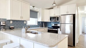 A modern kitchen with white cabinets, a stainless steel refrigerator, a microwave, and a coffee maker. - SALVO STARRY NIGHTS Beach House Bliss 5 min walk to beach (Salvo)