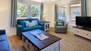 A living room with a blue sofa, a grey armchair, a wooden coffee table, a TV on a wooden stand, and a lamp on a side table. - SALVO STARRY NIGHTS Beach House Bliss 5 min walk to beach (Salvo)