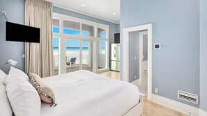 Ein Schlafzimmer mit einem Bett, einem Deckenventilator, einem Fernseher und Blick auf den Ozean durch große Fenster.