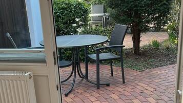 Een kamer met een deur die leidt naar een terras. Het terras heeft een terrastegel vloer, een tafel met stoelen en een barbecue.
