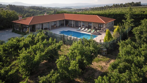 A large house with a swimming pool, surrounded by lush greenery and mountains in the background.