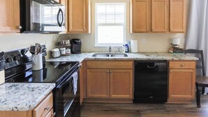 A kitchen with wooden cabinets, a black dishwasher, a granite countertop, and a window providing natural light. - Room for Everyone with 2 Townhomes and 6 Bedrooms! (Candler)