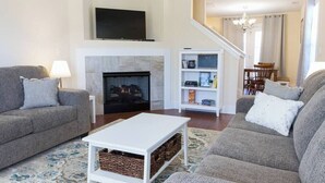 A living room with two grey sofas, a white coffee table, a fireplace, a bookshelf, and a TV mounted above the fireplace. - Room for Everyone with 2 Townhomes and 6 Bedrooms! (Candler)