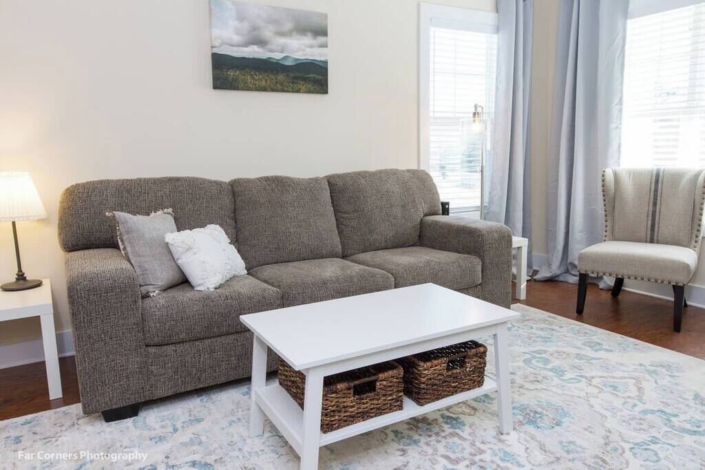 A living room with a grey sofa, a white coffee table, wicker baskets, a lamp, and a chair.