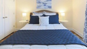 A neatly made bed with a blue blanket and pillows, two bedside lamps, and a painting on the wall. - Room for Everyone with 2 Townhomes and 6 Bedrooms! (Candler)