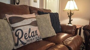 En brun lædersofa med dekorative puder, et lille bord med en lampe og en tæppe med mønster.