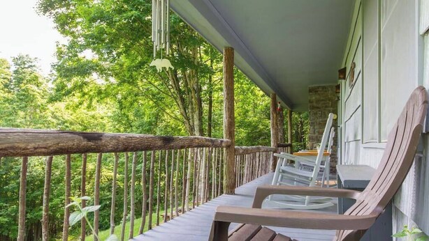 Eine Holzterrasse mit Bank, Tisch und Stühlen mit Blick auf einen üppigen grünen Wald.