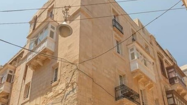Un immeuble à plusieurs étages, doté d’une façade en pierre, de balcons et d’un escalier menant à l’entrée.