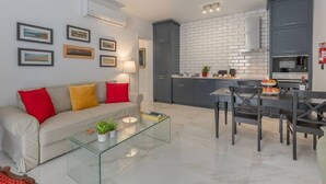 Un salon moderne avec une table basse en verre, un canapé avec des coussins rouges et un coin repas comprenant une table et des chaises.