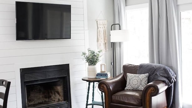 A living room with a fireplace, a leather sofa, a television mounted on the wall, and a small table with a plant and books. - *NEW* Cozy, Smart Condo| 10 mins to DT, Biltmore (Asheville)
