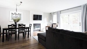 A modern living room with a dark sofa, a dining table with chairs, a chandelier, and a flat-screen TV mounted on the wall. - *Comfy Smart Condo|10 mins to DT & (Asheville)