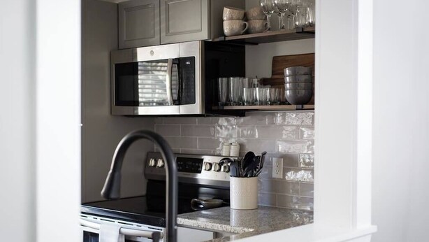 A kitchen with a stainless steel microwave, oven, and sink. There are shelves with glassware and a spice rack. - *Comfy Smart Condo|10 mins to DT & (Asheville)