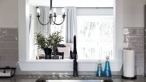 A kitchen with a sink, a chandelier, a window with curtains, and a potted plant. - *Comfy Smart Condo|10 mins to DT & (Asheville)