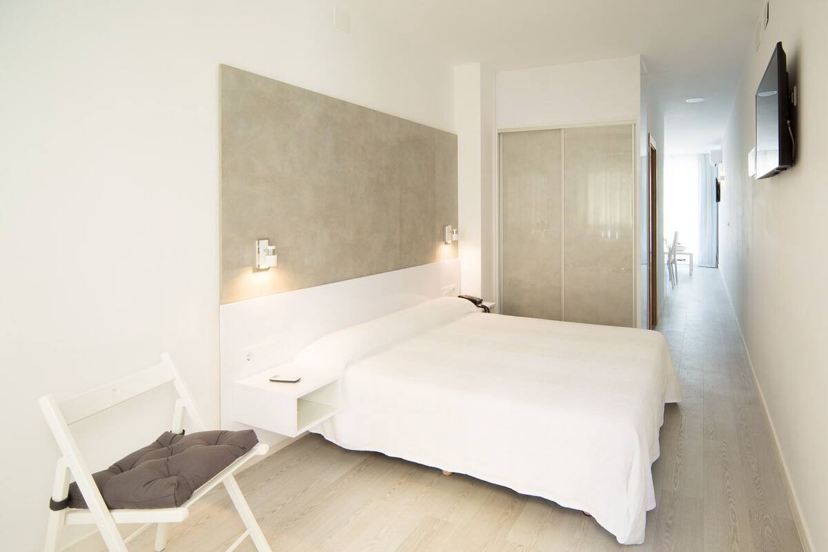 A modern bedroom with a large bed, a bedside table, a chair, and a wardrobe.