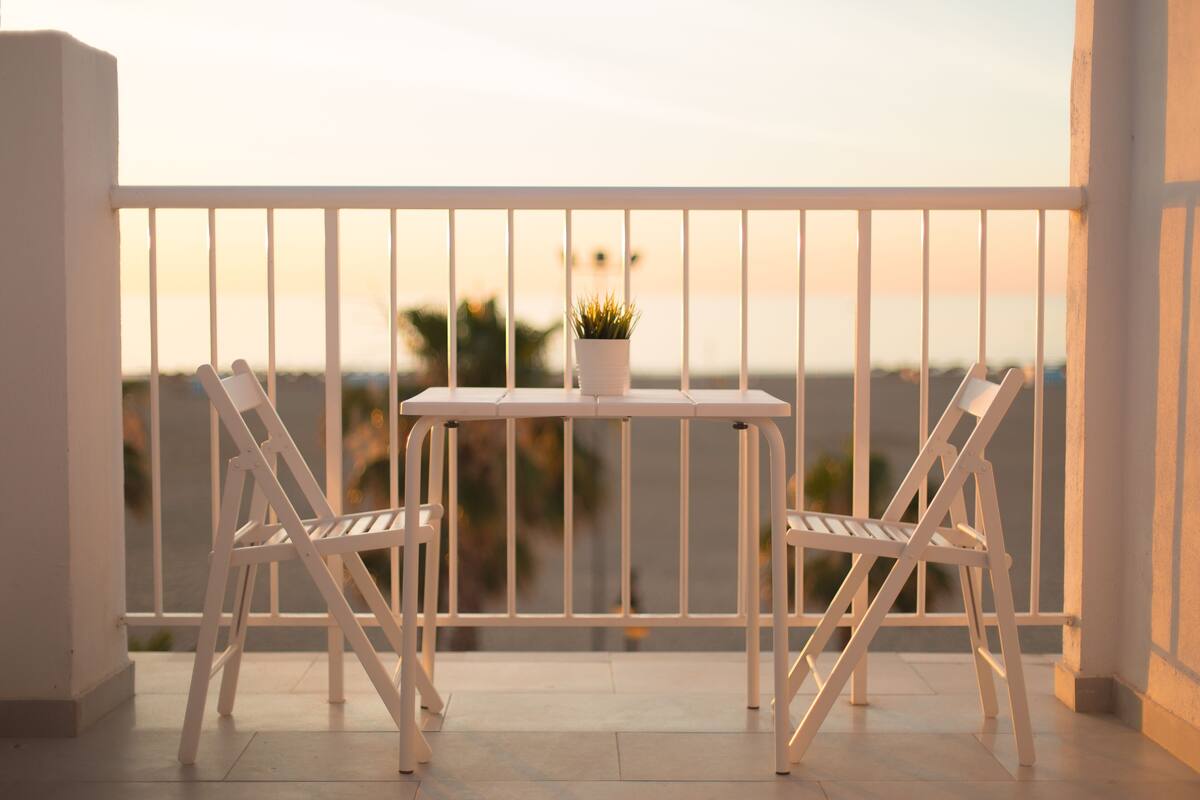 A balcony with two white chairs and a small table, overlooking a scenic view.