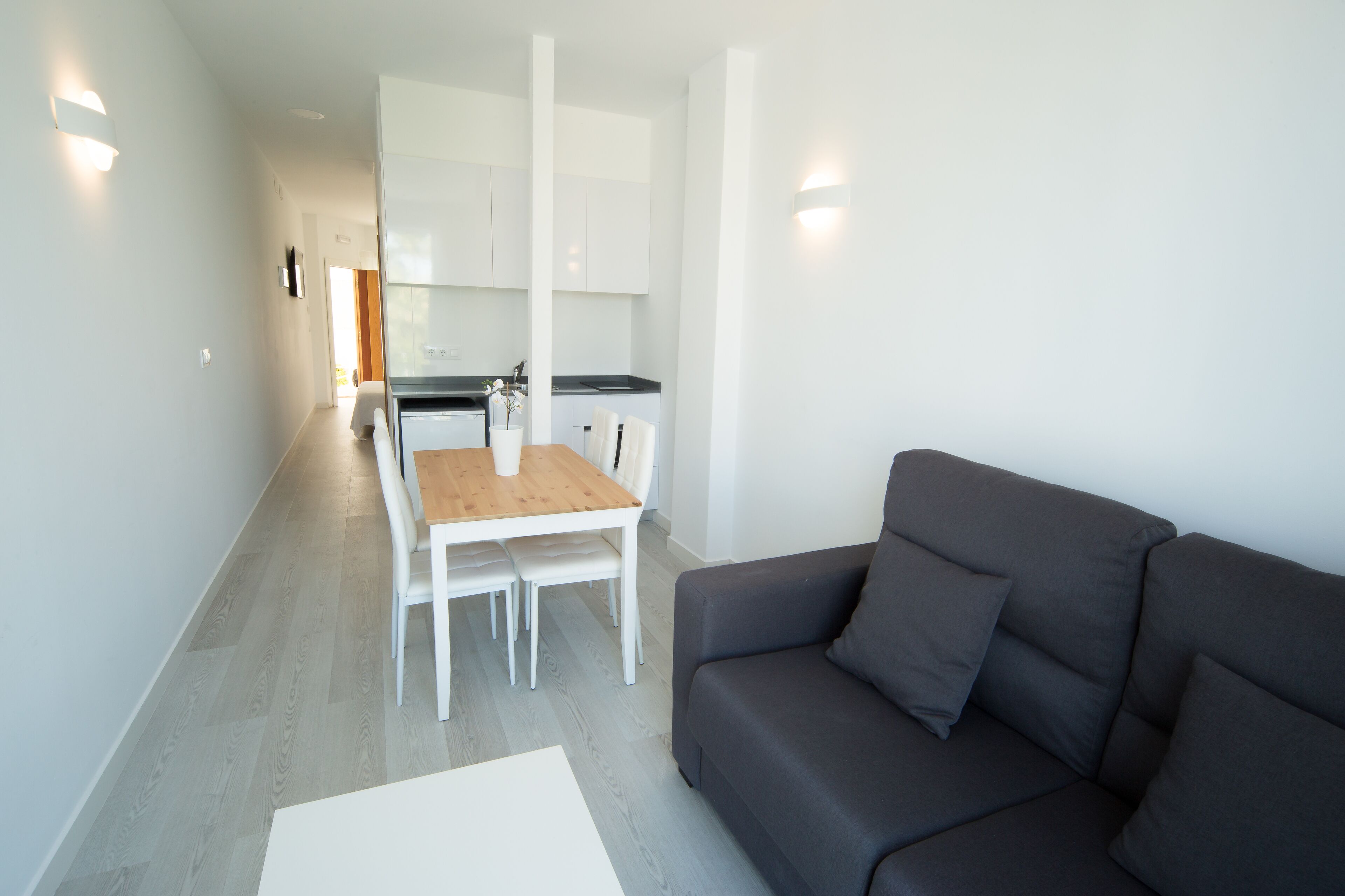 Una sala moderna con un sofá gris y una mesa de comedor de madera con sillas blancas.