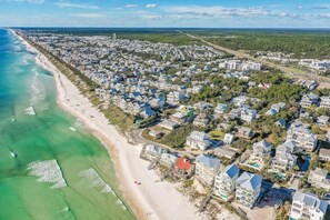 Vue aérienne d’une zone résidentielle côtière, avec des maisons le long de la plage et une vue dégagée sur l’océan.