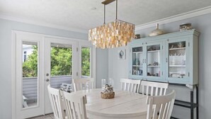 Un comedor con una mesa redonda, sillas blancas, una lámpara colgante y un armario azul claro con puertas de cristal.