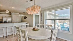 Una cocina amplia con armarios blancos, una mesa de comedor redonda y un gran ventanal con vistas al exterior.
