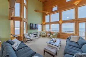 Relax in a spacious living area with a high ceiling and sea views, featuring a comfortable seating arrangement and a flat-screen TV.