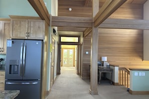 Kitchen area with a refrigerator, wooden cabinetry, and a hallway leading to a door.