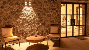 Una habitación acogedora con paredes de piedra, dos sillas de mimbre, una mesa de madera y un ventanal con vistas.