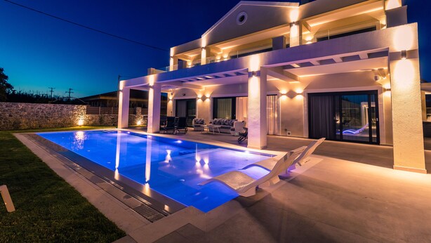 Una casa moderna de dos pisos con piscina, mobiliario exterior y un patio bien iluminado.