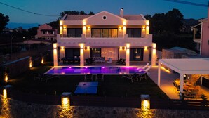 Una casa de dos pisos con piscina, mobiliario exterior y un patio cubierto.