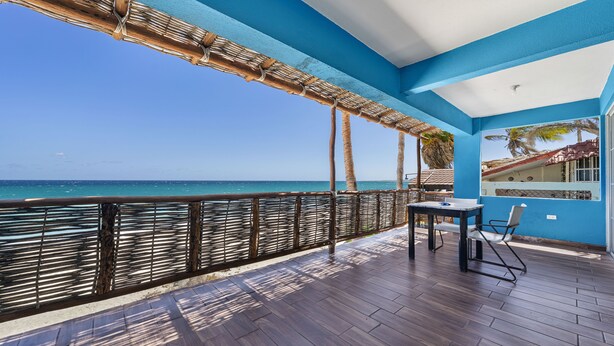 Un balcon avec vue sur l’océan, une table avec des chaises et un mur bleu avec une fenêtre.
