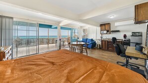 Une pièce spacieuse comprenant un grand lit, un coin repas et une cuisine. Elle dispose également d’un balcon avec vue sur l’océan.