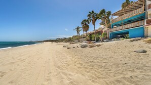 Une plage avec un bâtiment dont la façade est bleue et qui possède un balcon donnant sur l’océan.