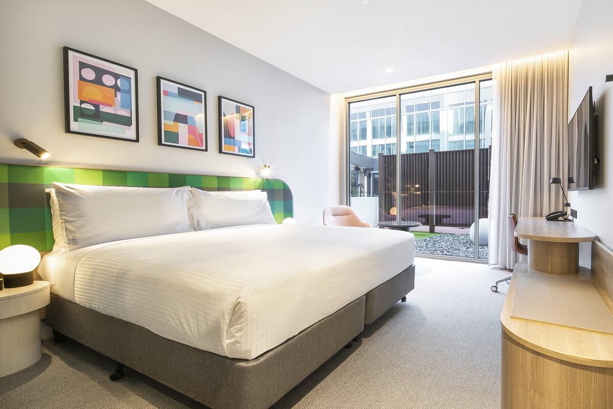 Una habitación de hotel moderna con una cama grande, un escritorio y vistas al exterior.