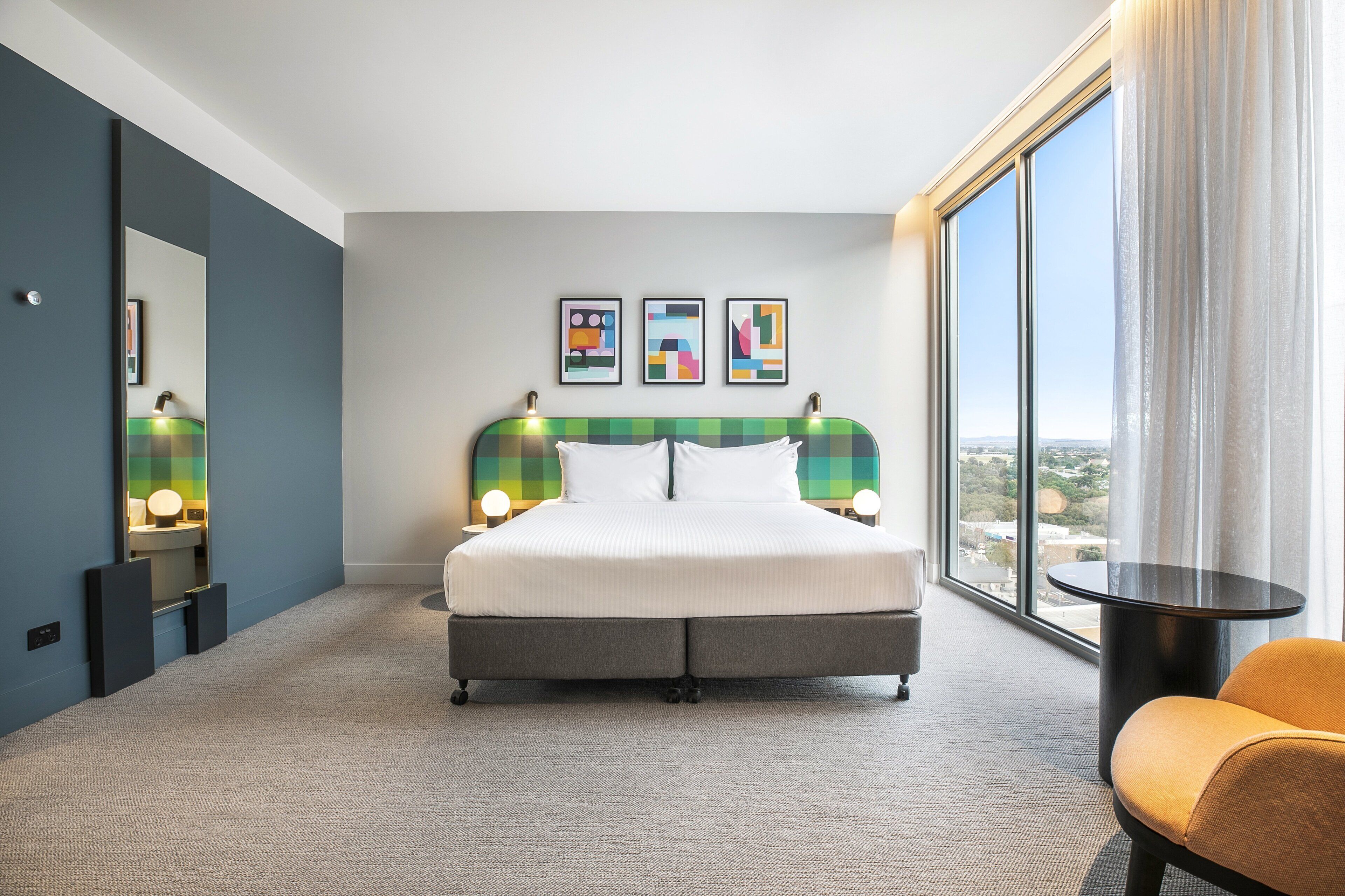 Habitación de hotel moderna con una cama grande, vistas a la ciudad y una pequeña mesa con una silla.
