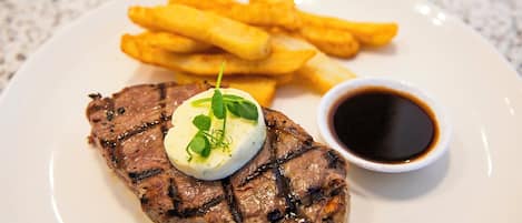 Un plato con un bistec a la parrilla, una guarnición de papas fritas y un recipiente pequeño de salsa.