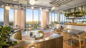 Um restaurante moderno com área de bar, janelas amplas e vista para a cidade.