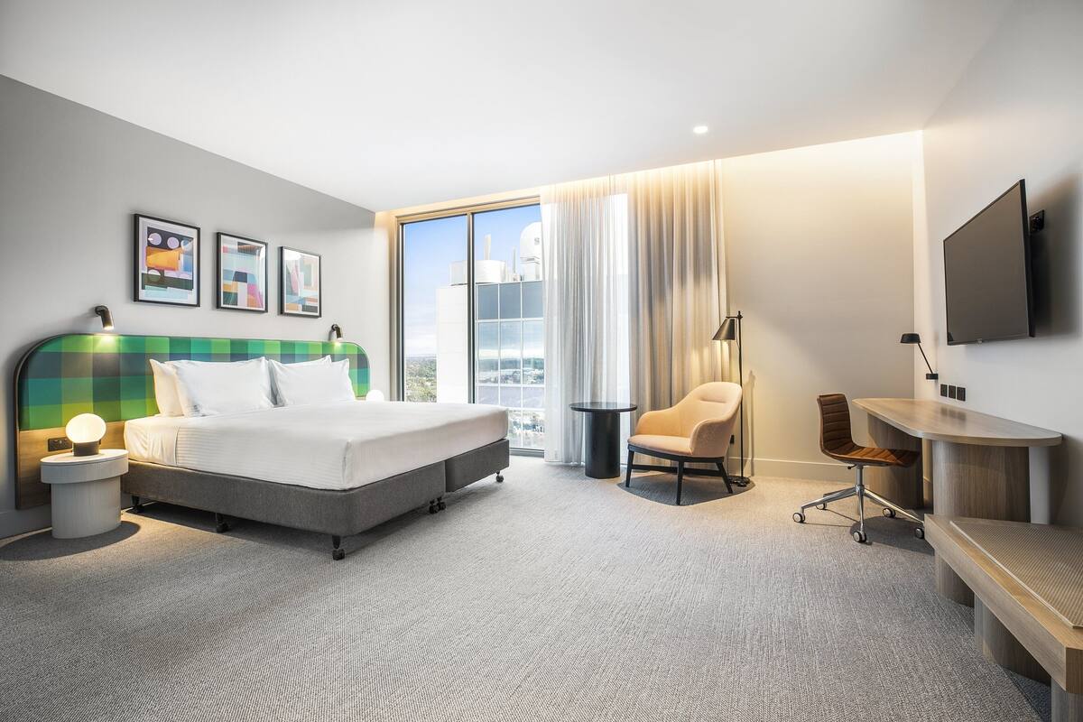 Una habitación de hotel moderna con una cama grande, un escritorio, una silla y un televisor en la pared.