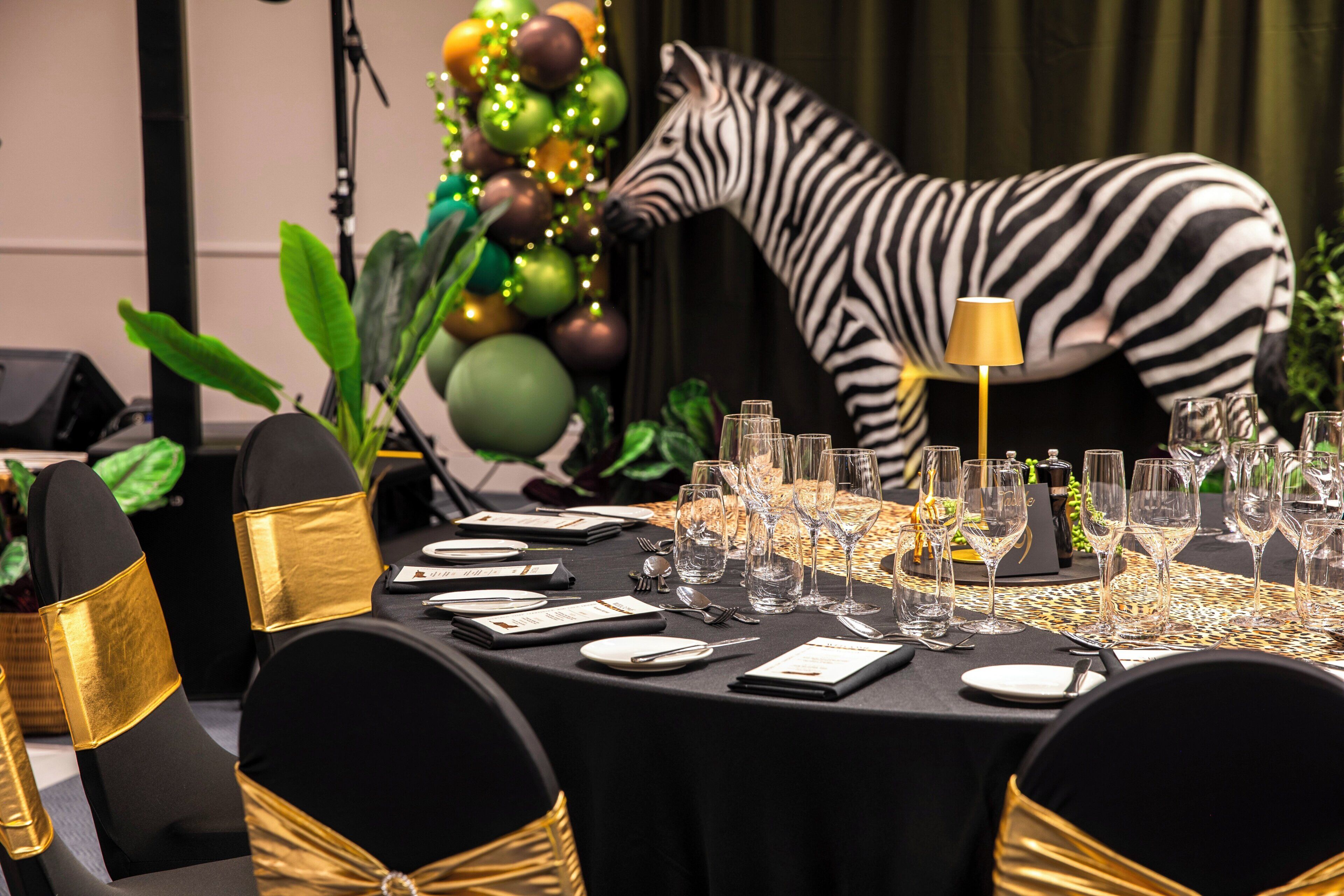 A table set for a formal event with a zebra decoration, gold chair accents, and a black tablecloth.