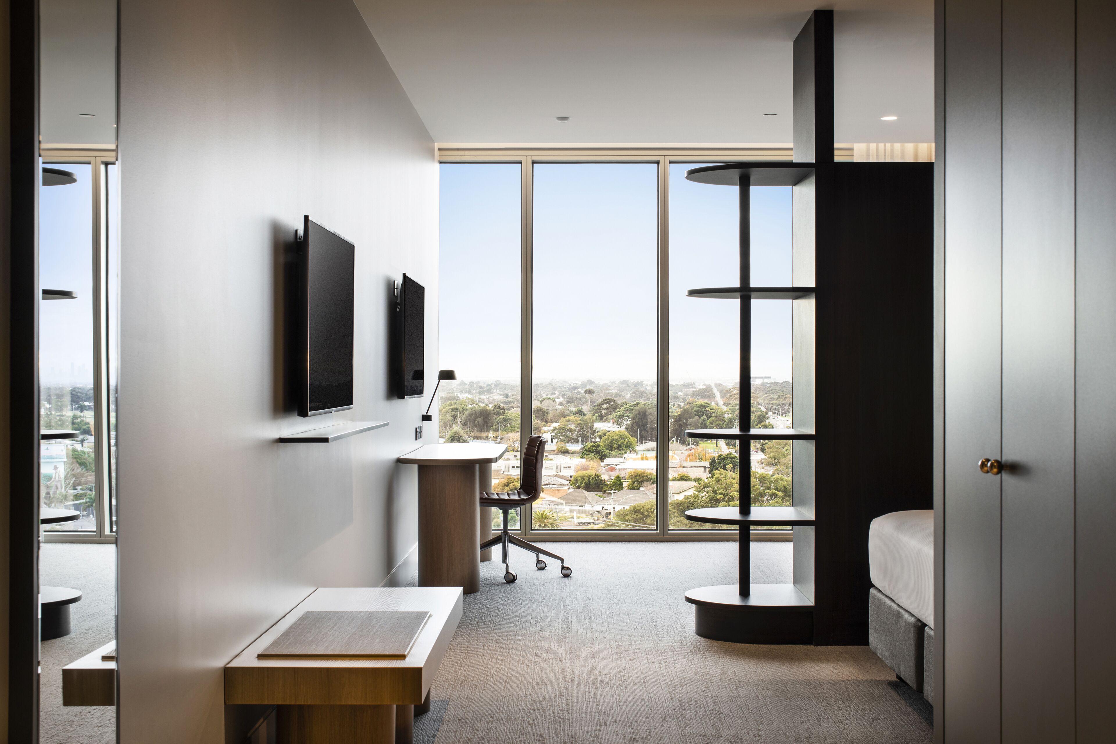Ein modernes Hotelzimmer mit großem Fenster, Schreibtisch, Stuhl, Bett und Wand-Fernseher.