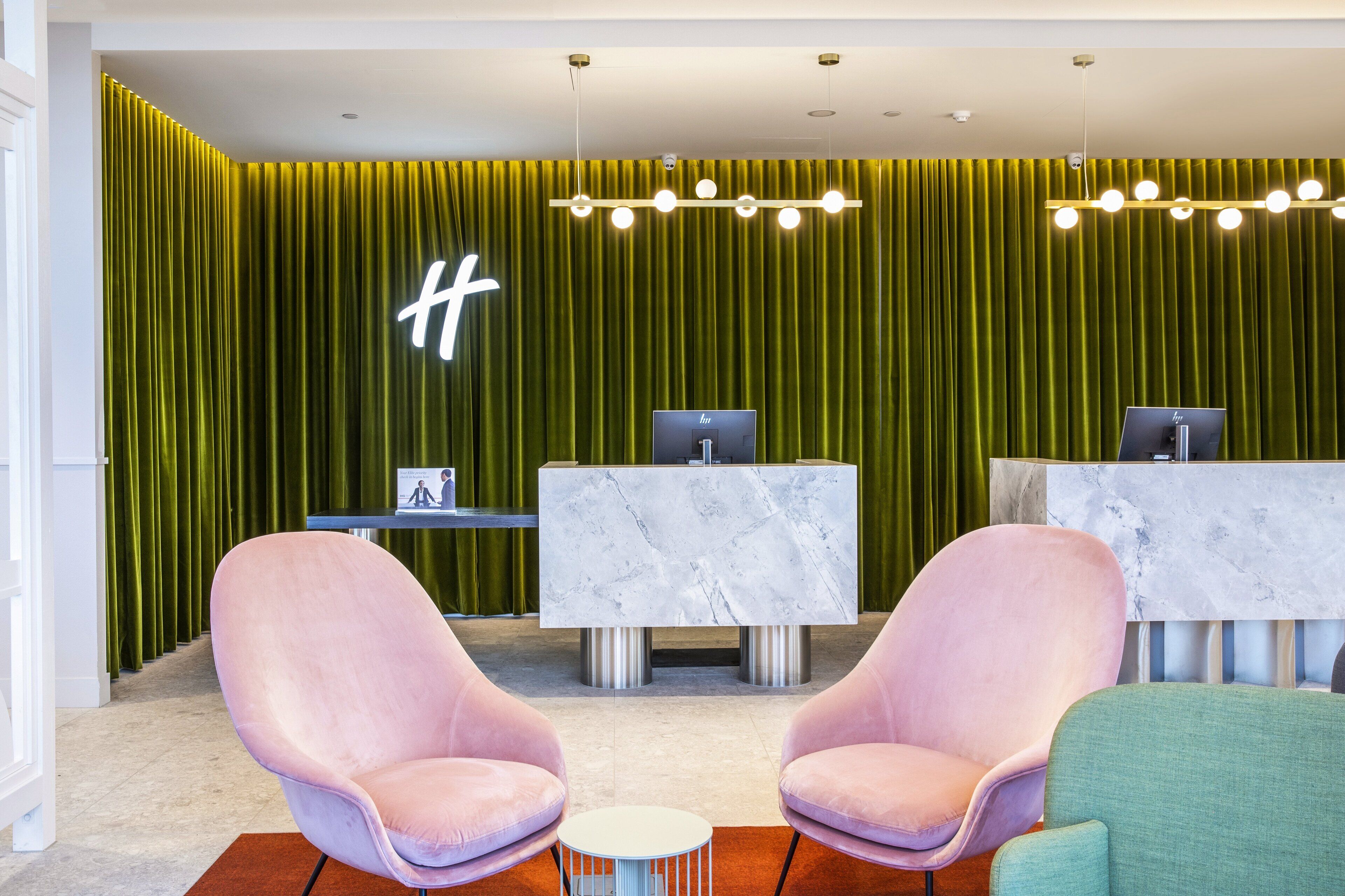 A reception area with green curtains, two reception desks, and two pink chairs.