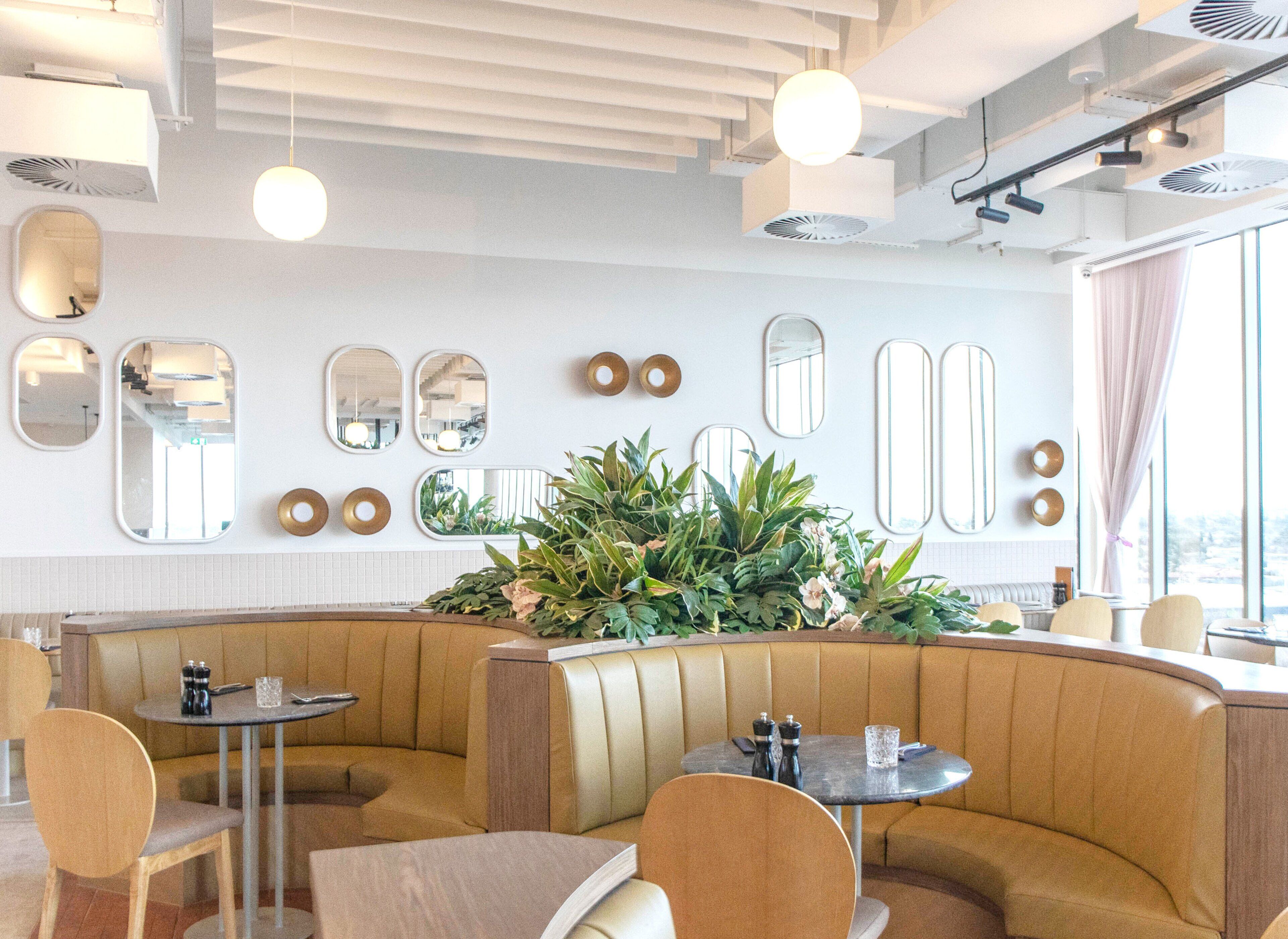 Un restaurante moderno con asientos tipo cabina, mesas redondas y un gran centro de mesa con plantas.