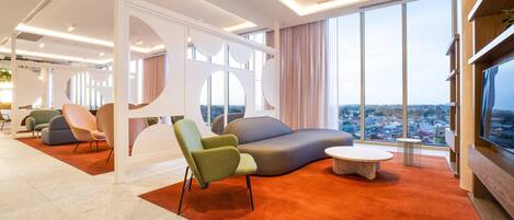 A modern hotel lobby with a large seating area, a view of the city, and a large window.