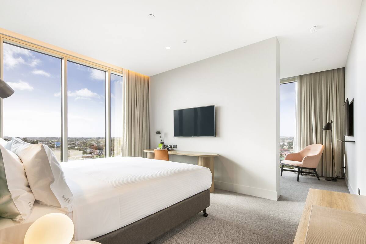 Habitación de hotel moderna con una cama grande, un escritorio, un televisor y vistas a la ciudad.